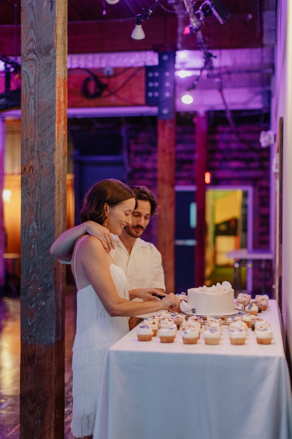 Couple cutting the cake with purple uplighting